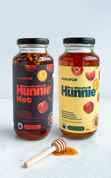 Two glass jars of 'Hunnie', one labeled as 'Hunnie' and the other as 'Hunnie Hot', alongside a wooden dipper. 